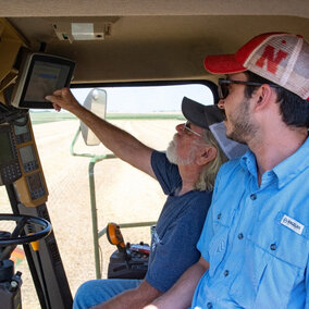 Two men inside tractor cab looking at software interface