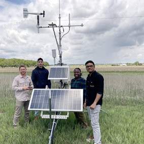 four people stand around weather station in field