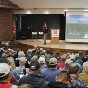 Audience attending a presentation in a lecture hall, with a speaker and a slide about nitrogen timing.