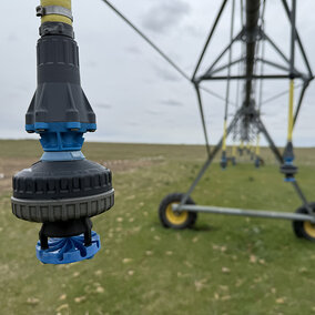 Sprinkler nozzle on an irrigation system in a grassy field under a cloudy sky.