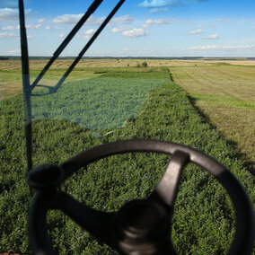 Farm field view through a tractor window, green crops and blue sky visible.
