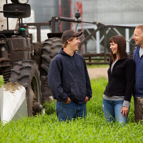 Couple and son laughing on farm beside tractor