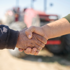 farmers shaking hands in front of tractor