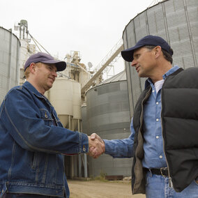 Two farmers standing in front of grain bins shaking hands