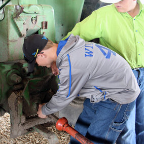 Two youth practicing proper connection procedures for a tractor PTO drive. Links to full article 'Tractor Safety Training Courses for Teen Farm/Ranch Workers'