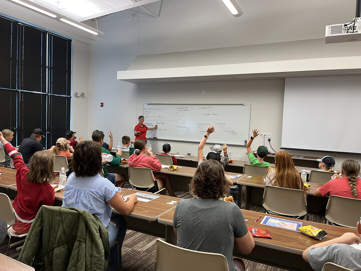 Woman stands at front of classroom full of children