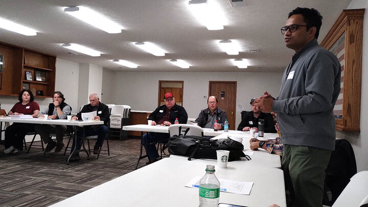 A presenter stands and addresses attendees during the Shell Creek Watershed workshop, with producers and stakeholders seated around tables in discussion