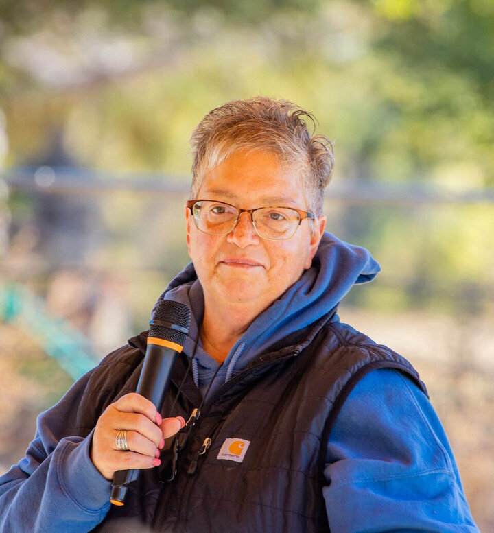 Kelly Huenink, keynote speaker for the 2025 Sidney Women in Ag Conference, holding a microphone and speaking outdoors in a casual setting.