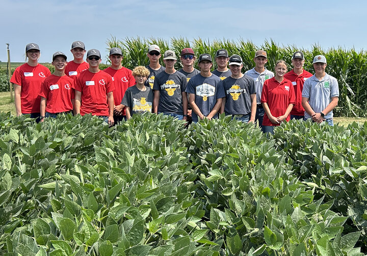 Group of Nebraska Youth Crop Scouting Competition participants standing in front of tall corn and behind lush soybean rows on a sunny day.