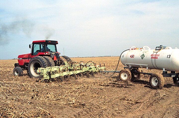 Red tractor pulls anhydrous ammonia tank through corn residue field