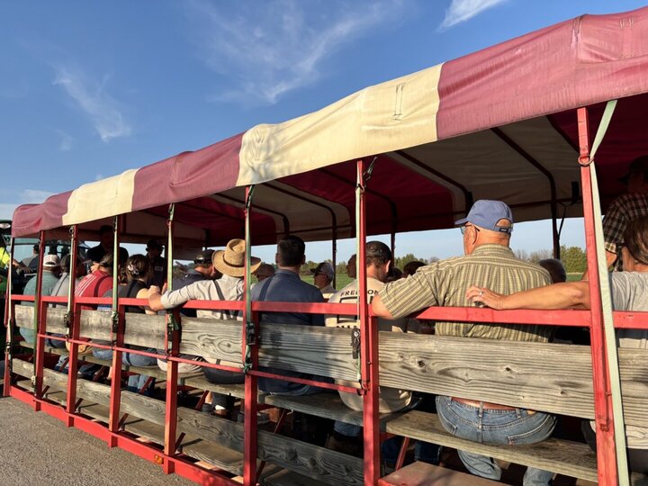 People seated on a wooden wagon covered by a red and white canopy under a sunny blue sky.