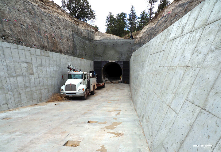 Concrete tunnel entrance with a parked utility truck, surrounded by rocky terrain and trees.