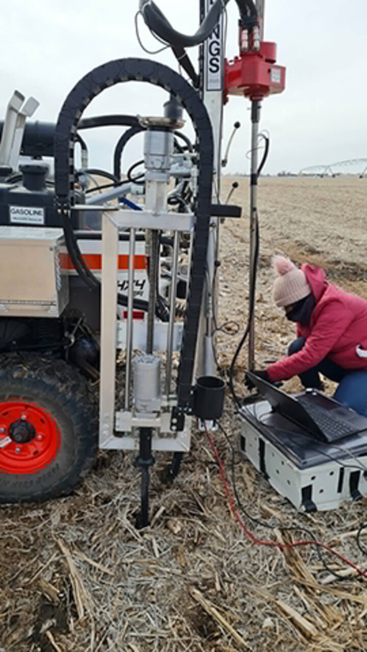 Person operating soil sampling equipment in a field with dry stalks.