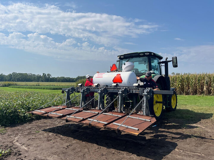 Tractor with sprayer attachment in a field under a cloudy sky.