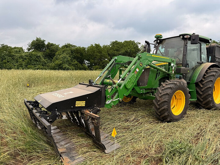 Green tractor with yellow rims operating in a grassy field under a cloudy sky.