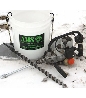 Five gallon bucket with large gas-powered drill laying on snowy ground and long large drill bit, laying crossed in front of it.