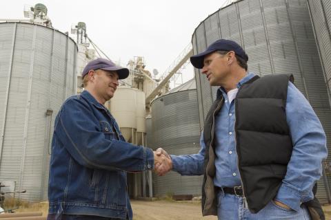 Two farmers standing in front of grain bins shaking hands