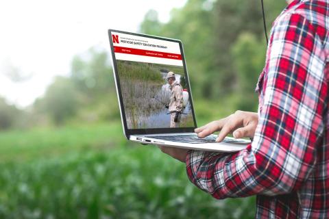 Man searching pesticide training website on laptop in field