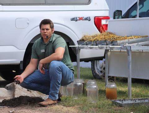 Man squats near demo table while speaking