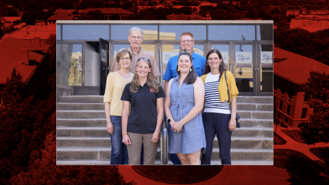 Six people stand on steps in front of building