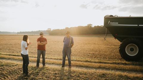 Three people stand in field near equipment