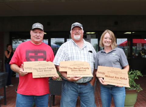 Trent Benzel, left, Steve Benzel and Michael Ann Relka stand with plaques